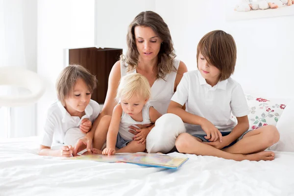 Junge Mutter, las ihren drei Kindern, Jungen, ein Buch in der Bibliothek — Stockfoto