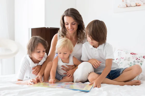 Jonge moeder, een boek lezen aan haar drie kinderen, jongens, in de worden — Stockfoto