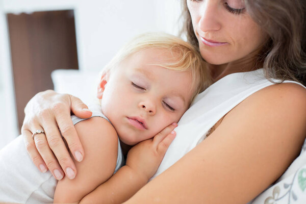 Young mother lying in bed with her sleeping toddler baby boy 