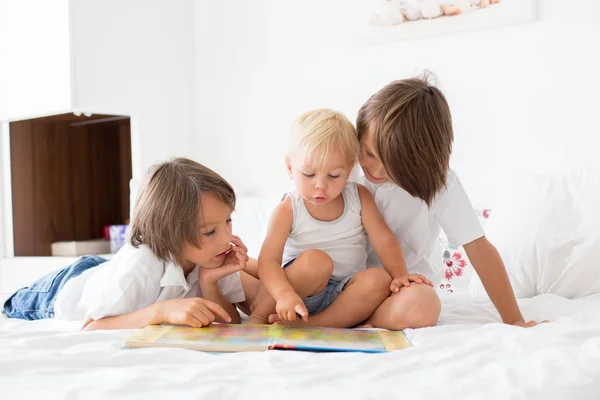 Три брата, милые дети, читают книгу в постели — стоковое фото