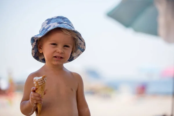 Édes szőke kisgyermek fiú, eaiting fagylaltot a strandon — Stock Fotó