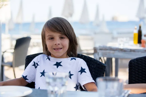 Dolce bambino preshcool, seduto in ristorante sulla spiaggia, in attesa di — Foto Stock