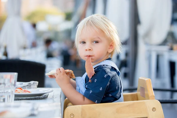 Ragazzo bambino carino, seduto sul seggiolone in un ristorante, mangiare — Foto Stock