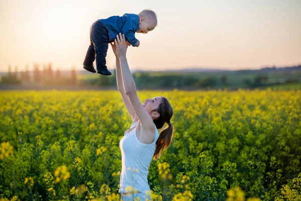 Jovem mãe segurando seu filho criança no campo de canola — Fotografia de Stock