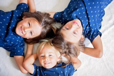 Çocuklar, kardeş kardeşler, beyaz battaniyenin üzerinde yerde yatıyorlar.,