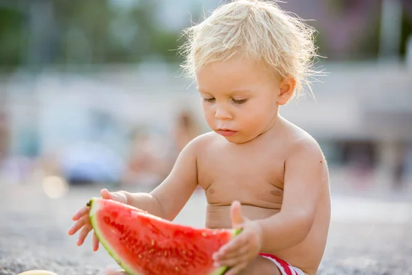 Cute toddler boy, blond child, eating watermelon on the beach co — Stock Photo, Image