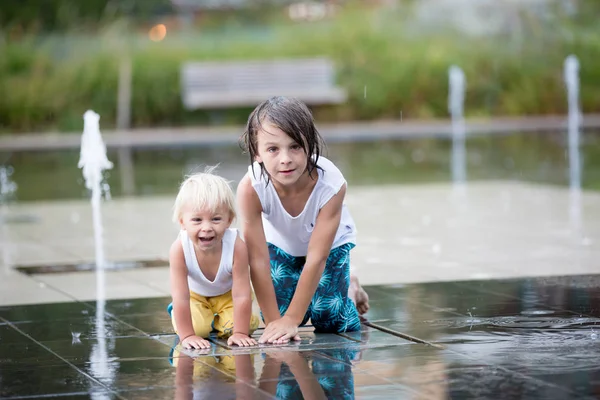 Lindo niño y hermanos mayores, jugando en una fuente de agua —  Fotos de Stock