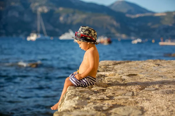 Dolce bambino ragazzo con cappello estivo e occhiali da sole, seduto sul — Foto Stock