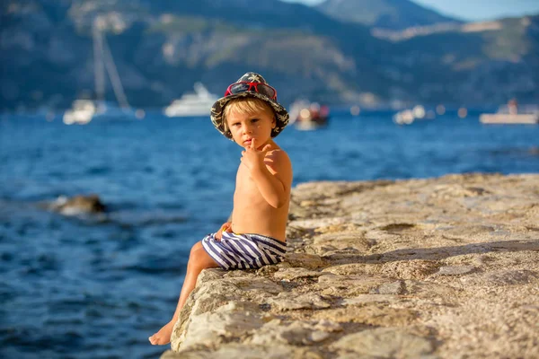 Dolce bambino ragazzo con cappello estivo e occhiali da sole, seduto sul — Foto Stock