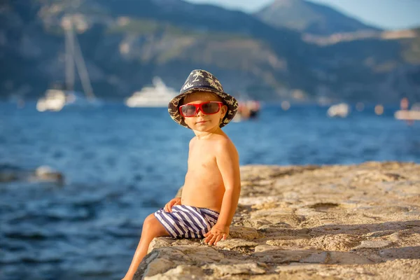 Dolce bambino ragazzo con cappello estivo e occhiali da sole, seduto sul — Foto Stock