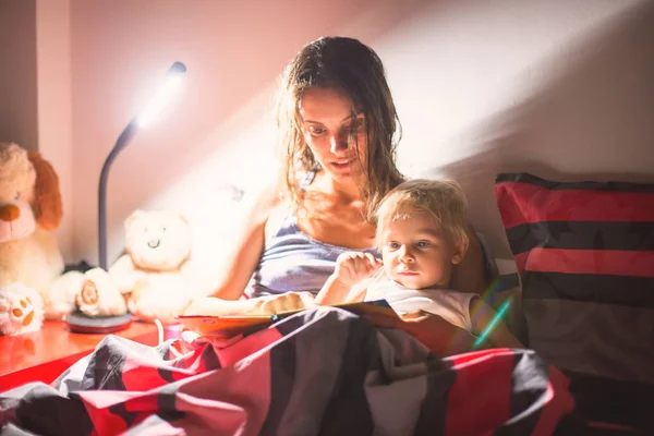 Mãe, ler um livro para o seu filho em casa à noite, perto — Fotografia de Stock