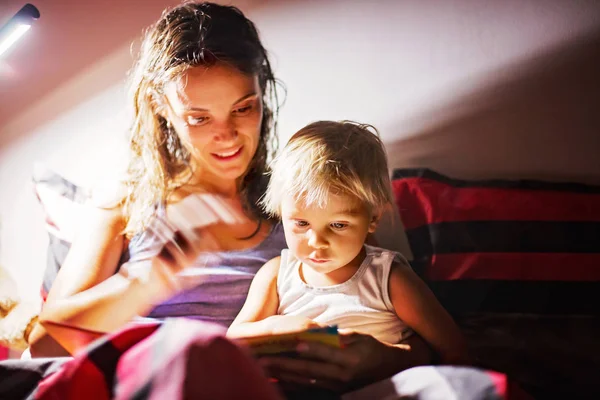 Mutter, die ihrem Kleinkind nachts zu Hause ein Buch vorliest, — Stockfoto