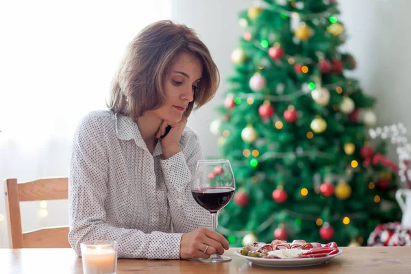 Jonge vrouw, drinken van wijn en met snack thuis op Kerstmis — Stockfoto