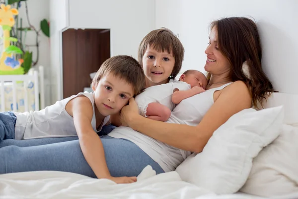 Jonge moeder liggend in bed met haar pasgeboren babyjongen en zijn olde — Stockfoto