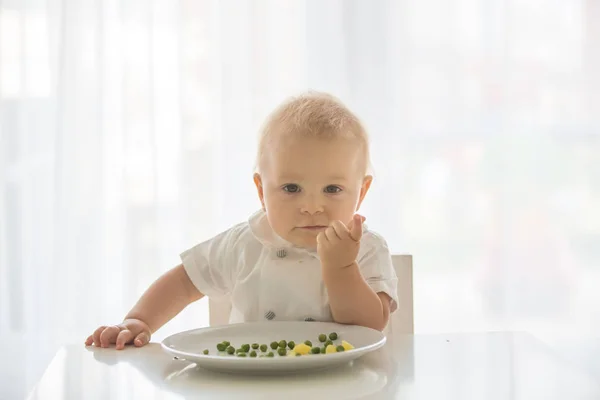 Criança, menino bonito em camisa branca, comer ervilha em casa — Fotografia de Stock