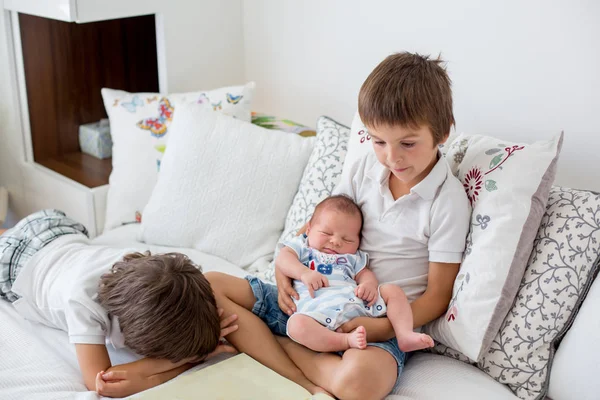 Süßer Vorschuljunge, der seinem neugeborenen Bruder ein Buch vorliest, sitt — Stockfoto