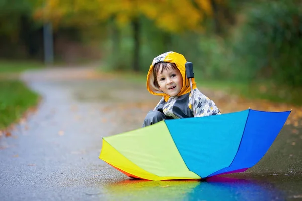 Милий хлопчик з барвистою веселкою парасолькою в дощовий день, маючи — стокове фото