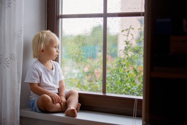 Sevimli küçük çocuk, pencere kalkanı üzerinde oturan, t bakarak