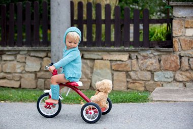 Örme kıyafeti ile sevimli yürümeye başlayan çocuk, bir q üç tekerlekli bisiklet sürme