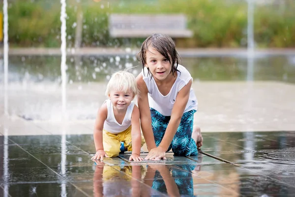 Lindo niño y hermanos mayores, jugando en una fuente de agua —  Fotos de Stock