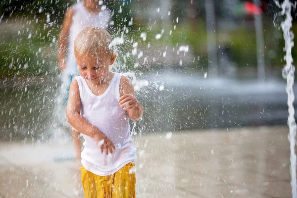 Menino bonito e irmãos mais velhos, brincando em fontes de jato — Fotografia de Stock