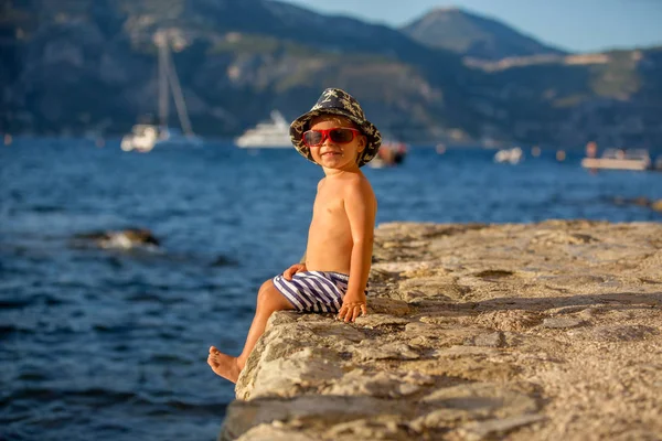 Sweet toddler boy with summer hat and sunglasses, sitting on the — Stock Photo, Image