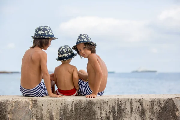 Tres niños, hermanos, sentados en una pared de hormigón en el muelle — Foto de Stock