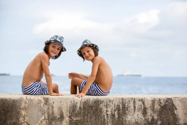Due bambini, fratelli maschi, seduti su un muro di cemento sul molo o — Foto Stock