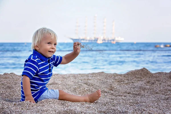 Bambino bambino, seduto sulla spiaggia, a guardare la nave illuminata in oc — Foto Stock