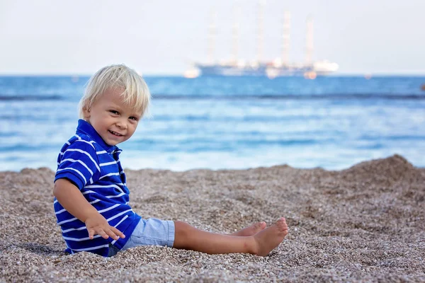 Peuter kind, zittend op het strand, kijkend naar verlicht schip in de OC — Stockfoto