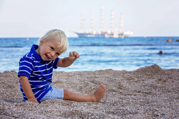 Bambino bambino, seduto sulla spiaggia, a guardare la nave illuminata in oc — Foto Stock