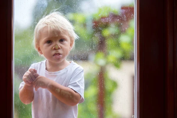 Cute little boy, looking at camera through glass door with rain — Stock Photo, Image