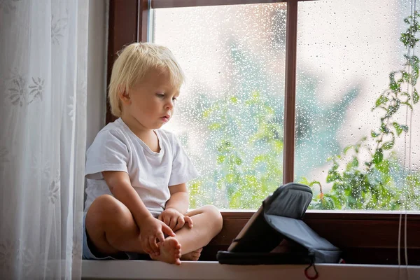 Bedårande liten pojke, sittande på fönstersköld, spela på Tablet — Stockfoto