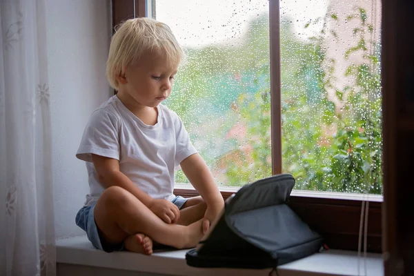 愛らしい小さな男の子、窓の盾に座って、タブレットで遊ぶ — ストック写真