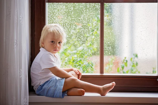 Adorable Little Boy, siedząc na tarczy okienne, patrząc przez t — Zdjęcie stockowe