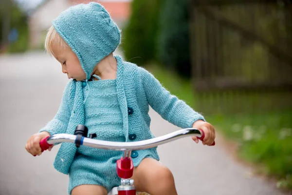 Bedårande småbarn pojke med stickade outfit, ridning trehjuling på en q — Stockfoto