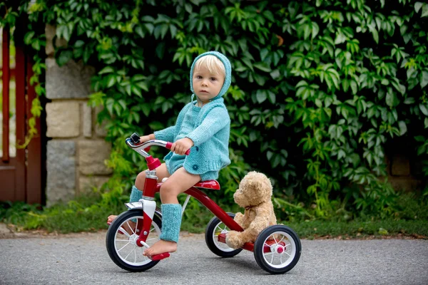 Adorabile bambino con vestito a maglia, triciclo a cavallo su un q — Foto Stock