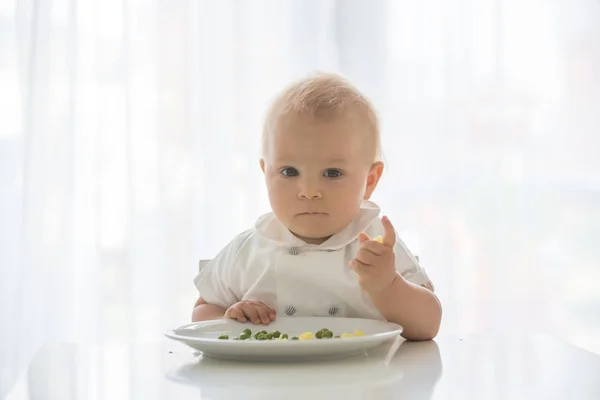 Criança, menino bonito em camisa branca, comer ervilha em casa — Fotografia de Stock