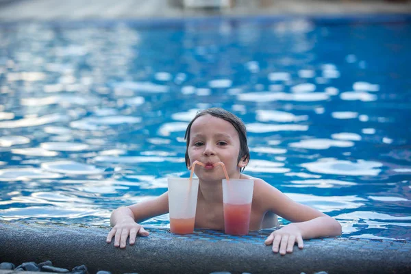 Симпатичный мальчик, пьет коктейль в бассейне во время отпуска в тропиках — стоковое фото