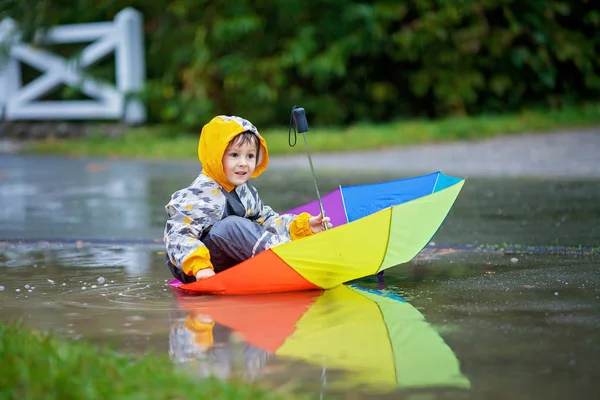 Niedlicher Junge mit buntem Regenbogen-Regenschirm an einem regnerischen Tag — Stockfoto