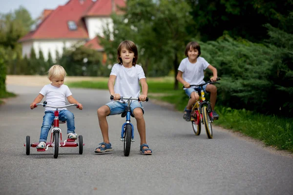 Трое детей, езда на велосипеде, трицикле и балансовом велосипеде по ул. — стоковое фото