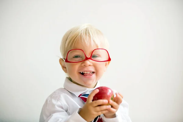 Söt unge, bära glasögon och äta äpple, klädd för första da — Stockfoto