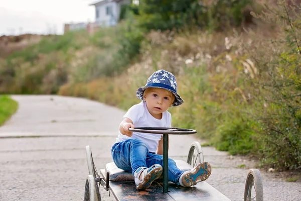 Очаровательный малыш, ездит на старой ретро машине с четырьмя колесами — стоковое фото