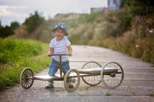 愛らしい幼児の少年、4つの車輪を持つ古いレトロな車に乗って — ストック写真