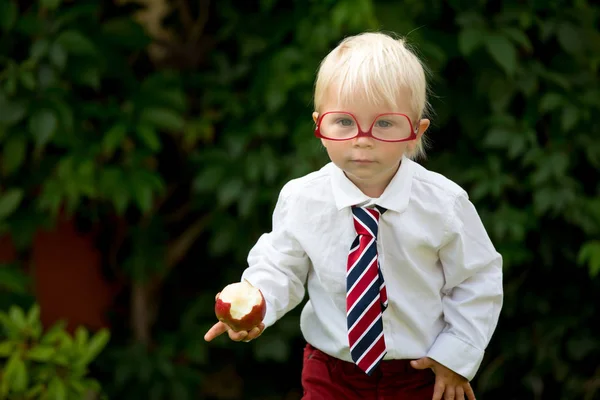 Söt unge, bära glasögon och äta äpple, klädd för första da — Stockfoto