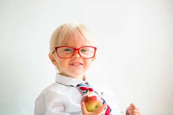 Roztomilý kluk, nosí brýle a jíst jablko, oblečené na první da — Stock fotografie