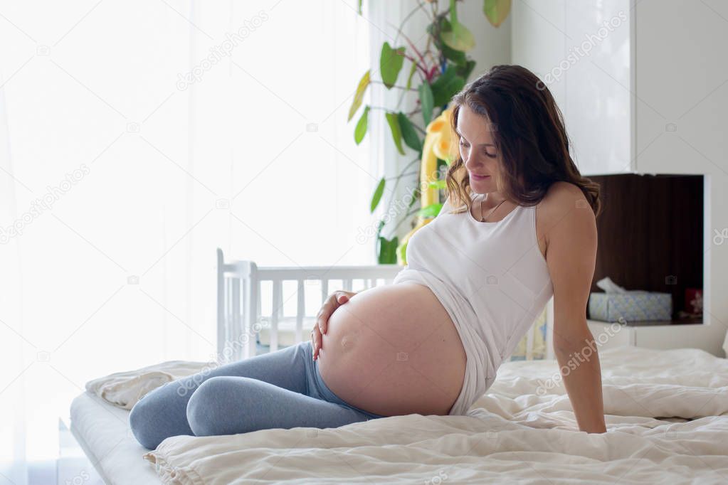 Happy young beautiful pregnant woman, sitting on bed in bedroom