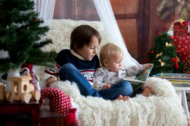 Sevimli çocuk noel t altında sandalyede oturan kitap okuma