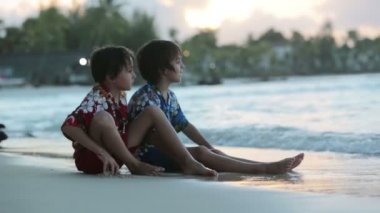 Mutlu güzel moda ailesi, çocuklar, Hawaii gömlekleri giyip gün batımında sahilde birlikte oynuyorlar, ailelerin neşeli tatili.