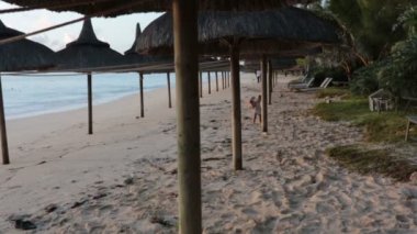 Küçük yürümeye başlayan çocuk, gün doğumunda sahilde oyuncak ayı ile oynarken, plajda Şemsiyeler